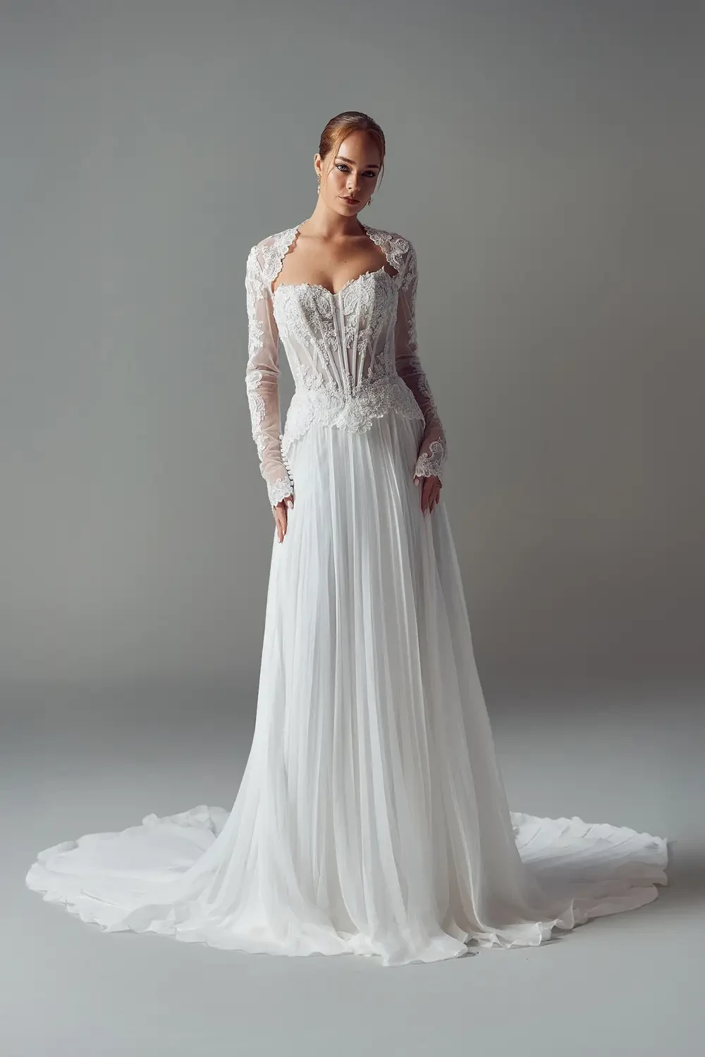 A model wearing a white wedding dress with intricate lace details and a long train.