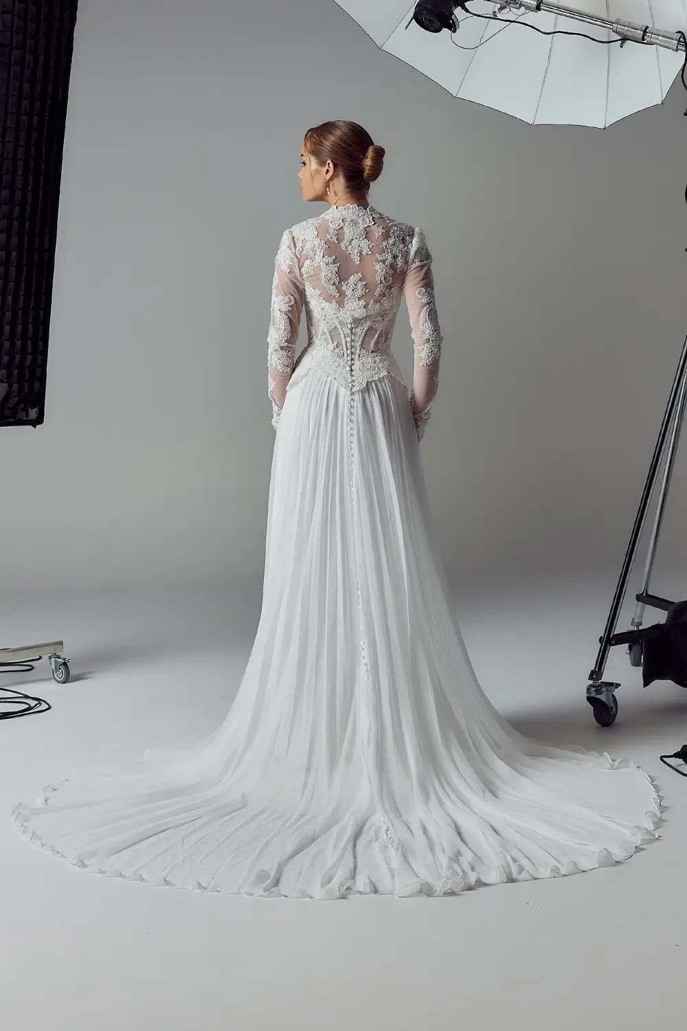A model wearing a white wedding dress with intricate lace details and a long train.